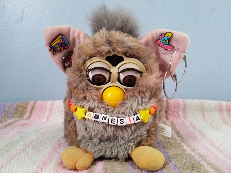 A grey-brown Furby with music-related pins