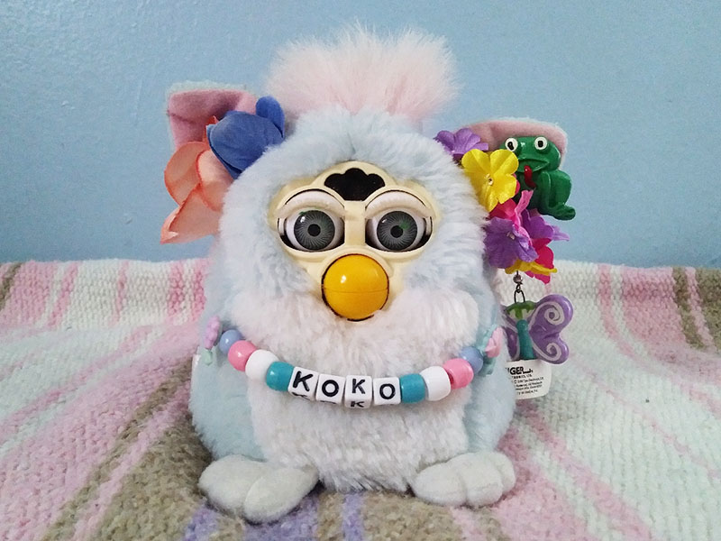 A baby blue Furby with flowers in his ears