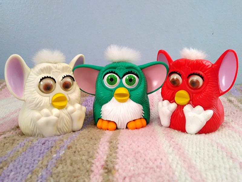 Three small plastic Furby toys- one white, teal, and red