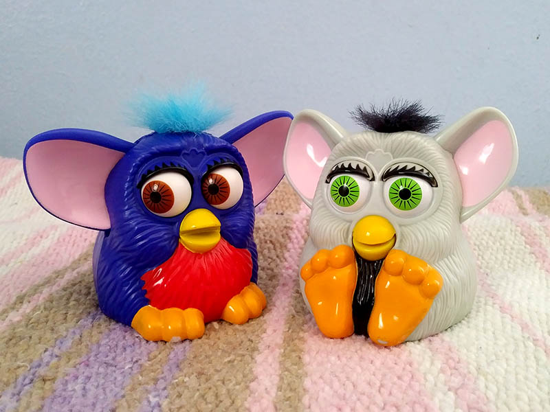 Two small plastic Furby toys- one blue and red, the other grey