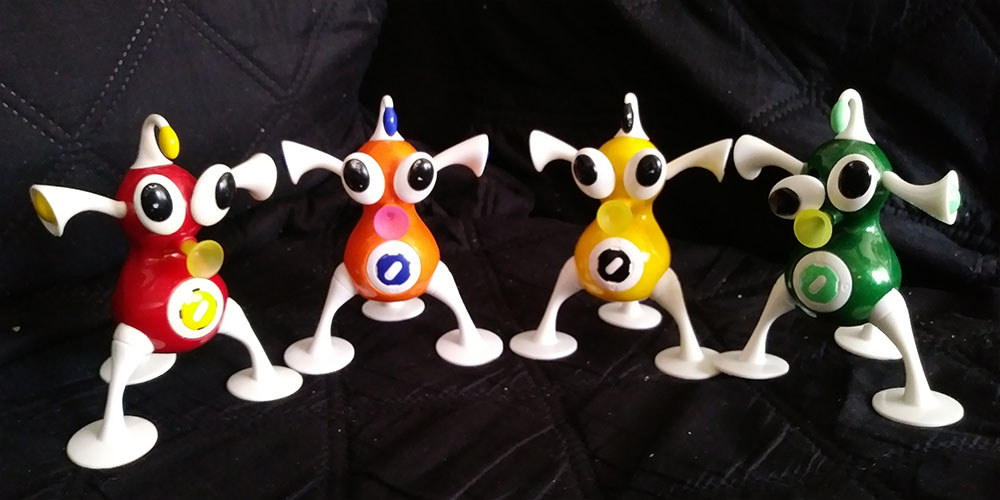 A row of 4 iZ toys in rainbow order, from red to green.