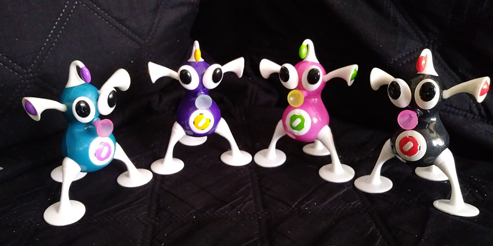 A row of 4 iZ toys in rainbow order, from blue to black.